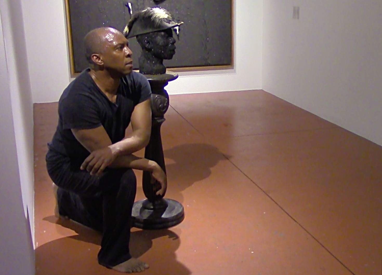 Boris Willis walking through a gallery beside Radcliffe Bailey's work