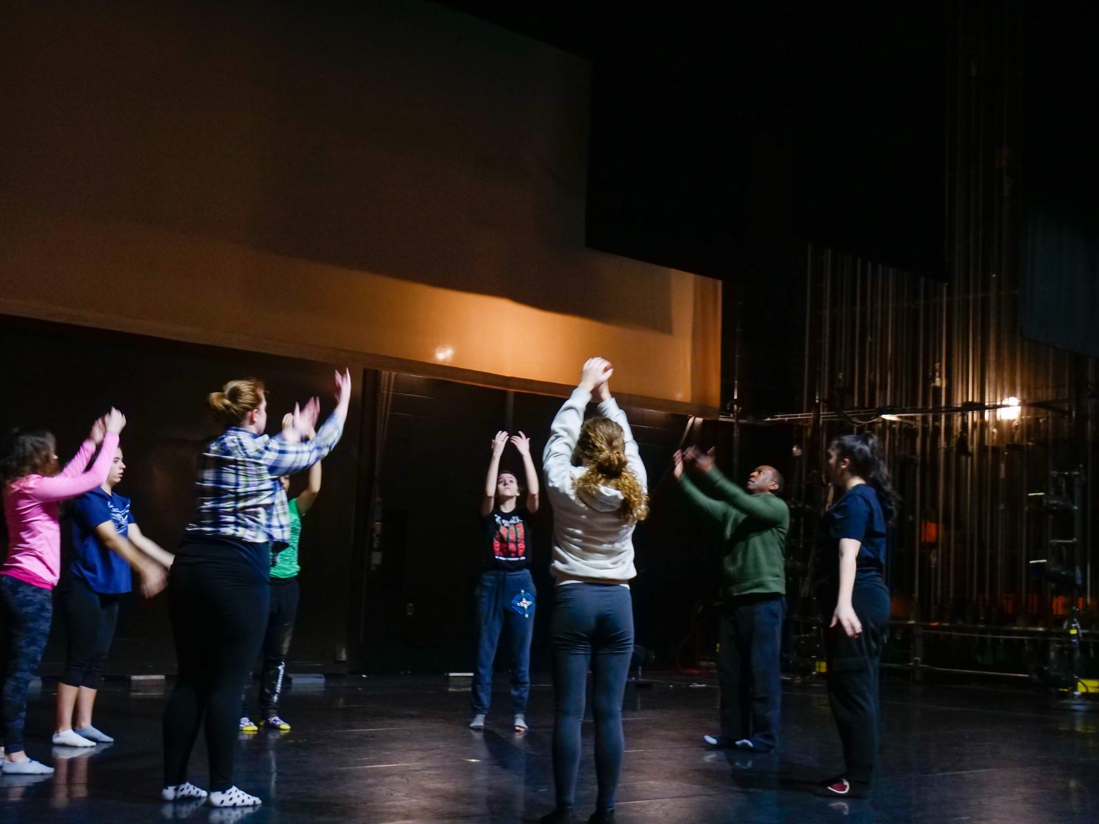 A cluster of dancers with arms raised overhead, gathered mid-stage